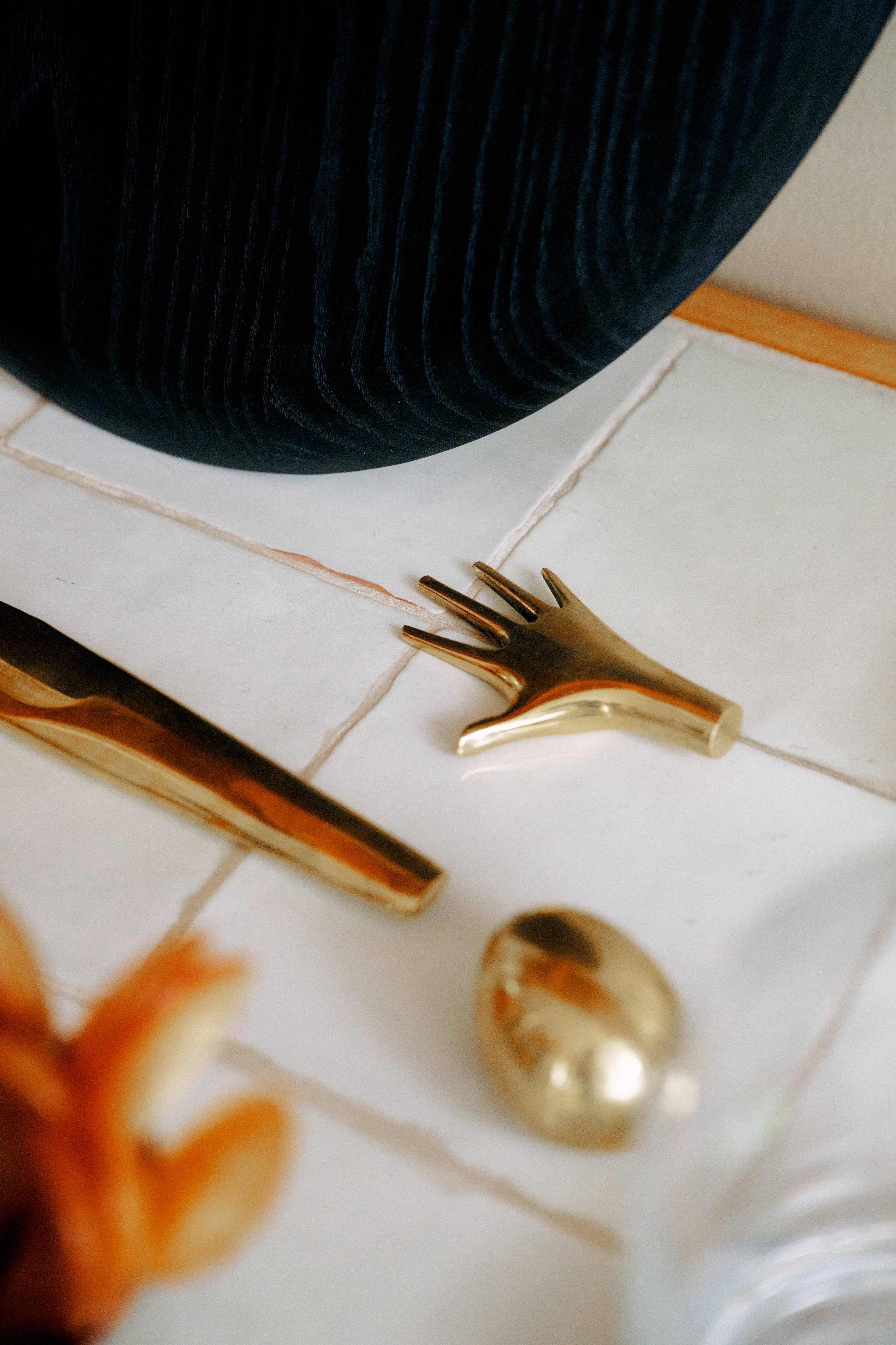 A Hand Paperweight in solid brass—evocative of Viennese modernism—rests alongside other brass forms on a white tiled surface near a dark textured fabric. Crafted by the Auböck workshop, these pieces exemplify timeless craftsmanship.