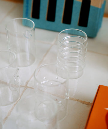 A set of six Deco Shot Glasses is arranged on a tiled surface, with a cardboard box and an orange object partially visible in the background—perfect for serving limoncello or grappa.