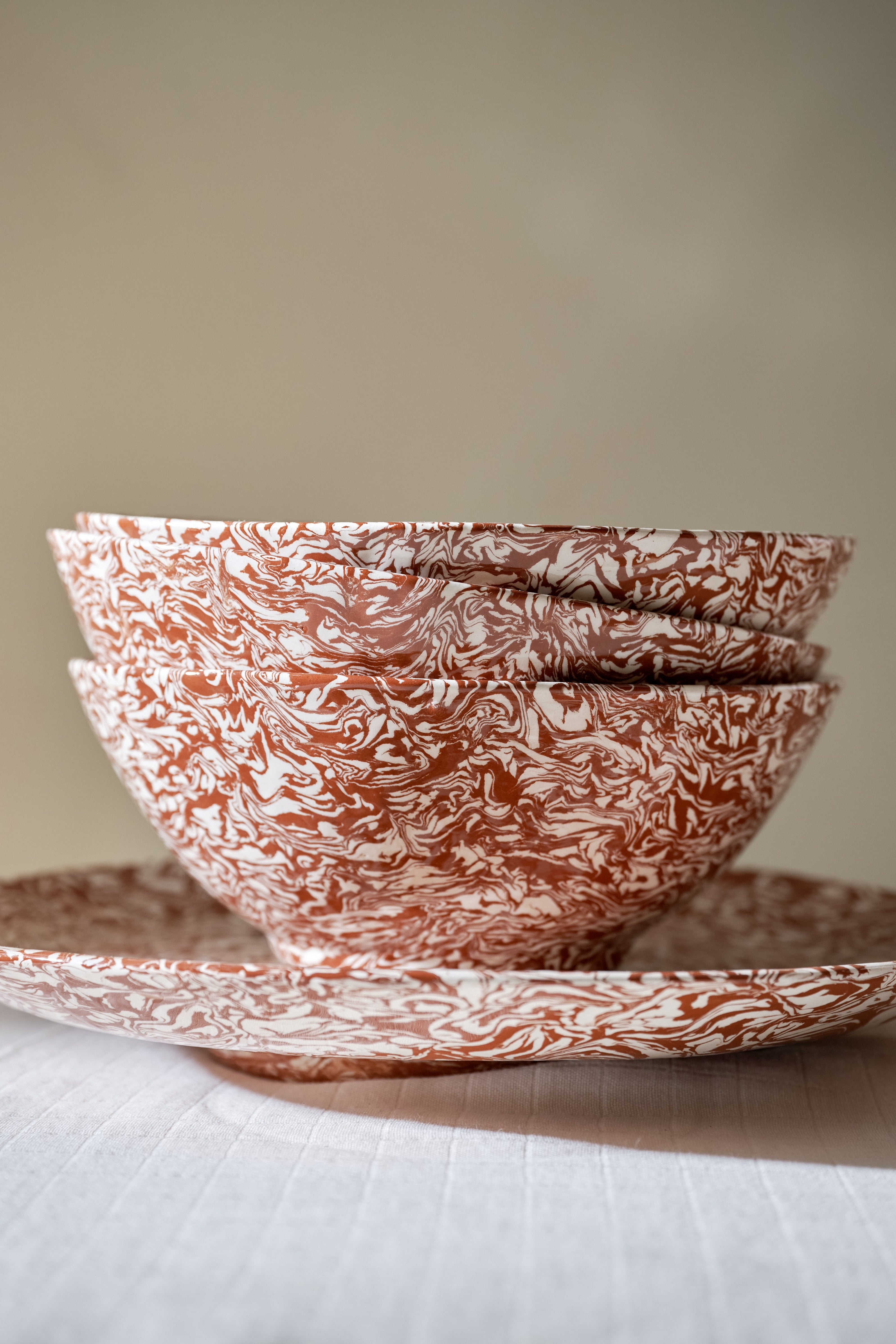 Three stacked Celine Salad Bowls, featuring a striking marbled red and white pattern, sit inside a matching plate on a white tablecloth against a neutral background.