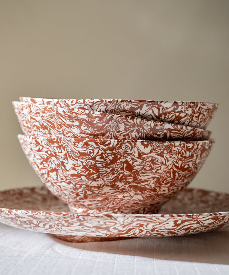 Three stacked Celine Salad Bowls, featuring a striking marbled red and white pattern, sit inside a matching plate on a white tablecloth against a neutral background.