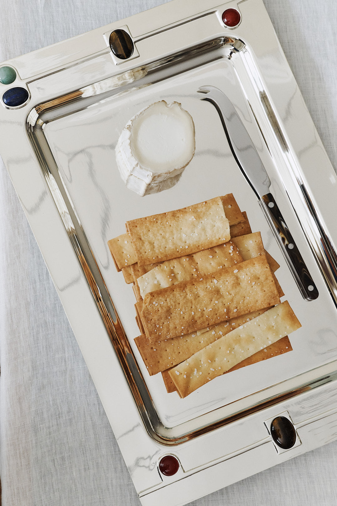 A Verola Rectangle Tray elegantly presents a round of goat cheese, a cheese knife, and several neatly arranged rectangular crackers.