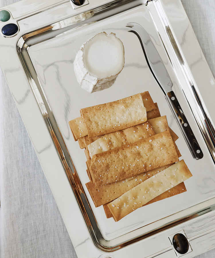 A Verola Rectangle Tray elegantly presents a round of goat cheese, a cheese knife, and several neatly arranged rectangular crackers.