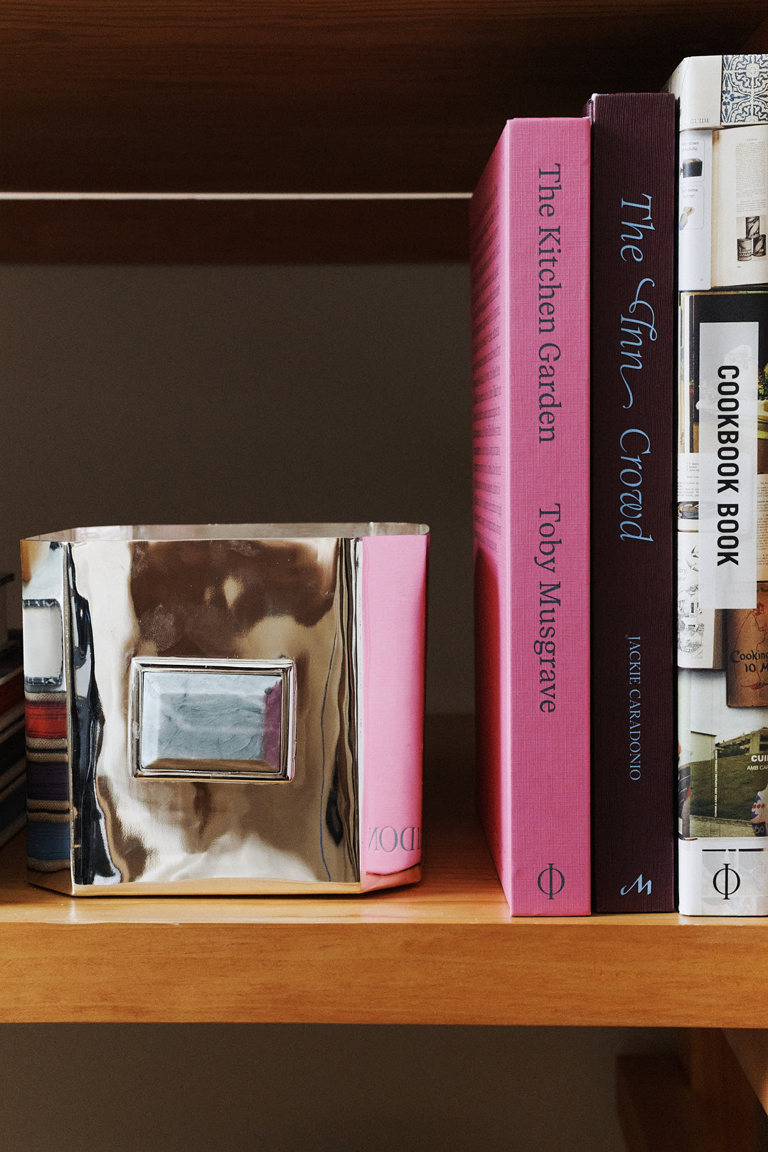 A silver decorative box sits on a wooden shelf next to pink and brown cookbooks, including The Kitchen Garden, a book packed with inspiring gardening tips.