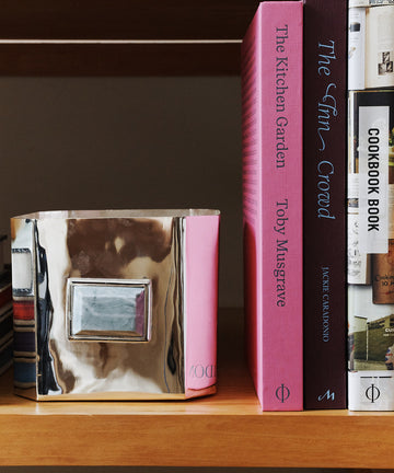 A silver decorative box sits on a wooden shelf next to pink and brown cookbooks, including The Kitchen Garden, a book packed with inspiring gardening tips.