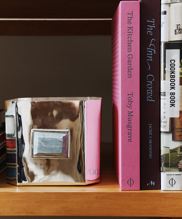 A silver decorative box sits on a wooden shelf next to pink and brown cookbooks, including The Kitchen Garden, a book packed with inspiring gardening tips.