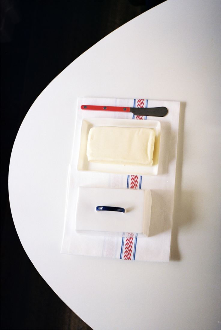 A Butterdish holding a stick of butter and a bar of soap, each with a knife, sits on a folded towel atop a white table, capturing elegant simplicity.