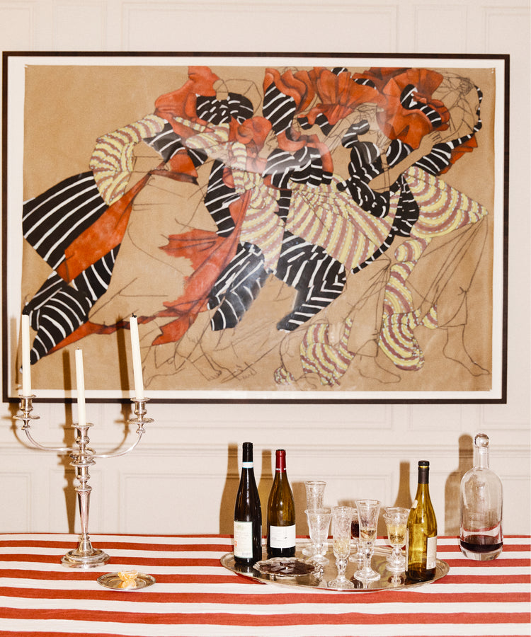 A Striped Tablecloth in festive red and white covers the table, which holds wine bottles, glasses, a decanter, and a silver candelabra; above hangs a large abstract painting.