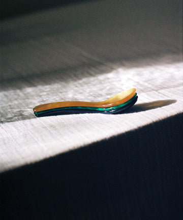 The Piccolo Spoon rests on a textured, sunlit tablecloth with its shadow to the right—ideal for soft boiled eggs and conveniently dishwasher safe.