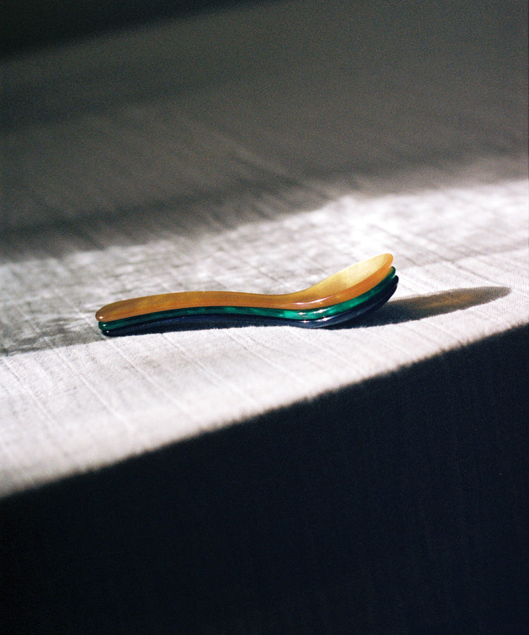 The Piccolo Spoon rests on a textured, sunlit tablecloth with its shadow to the right—ideal for soft boiled eggs and conveniently dishwasher safe.