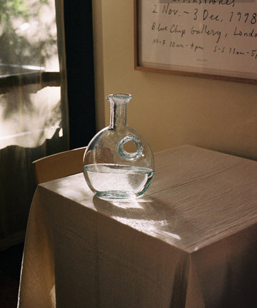 Alma Decanter, half-filled with water, sits on tablecloth in a rustic dining room.