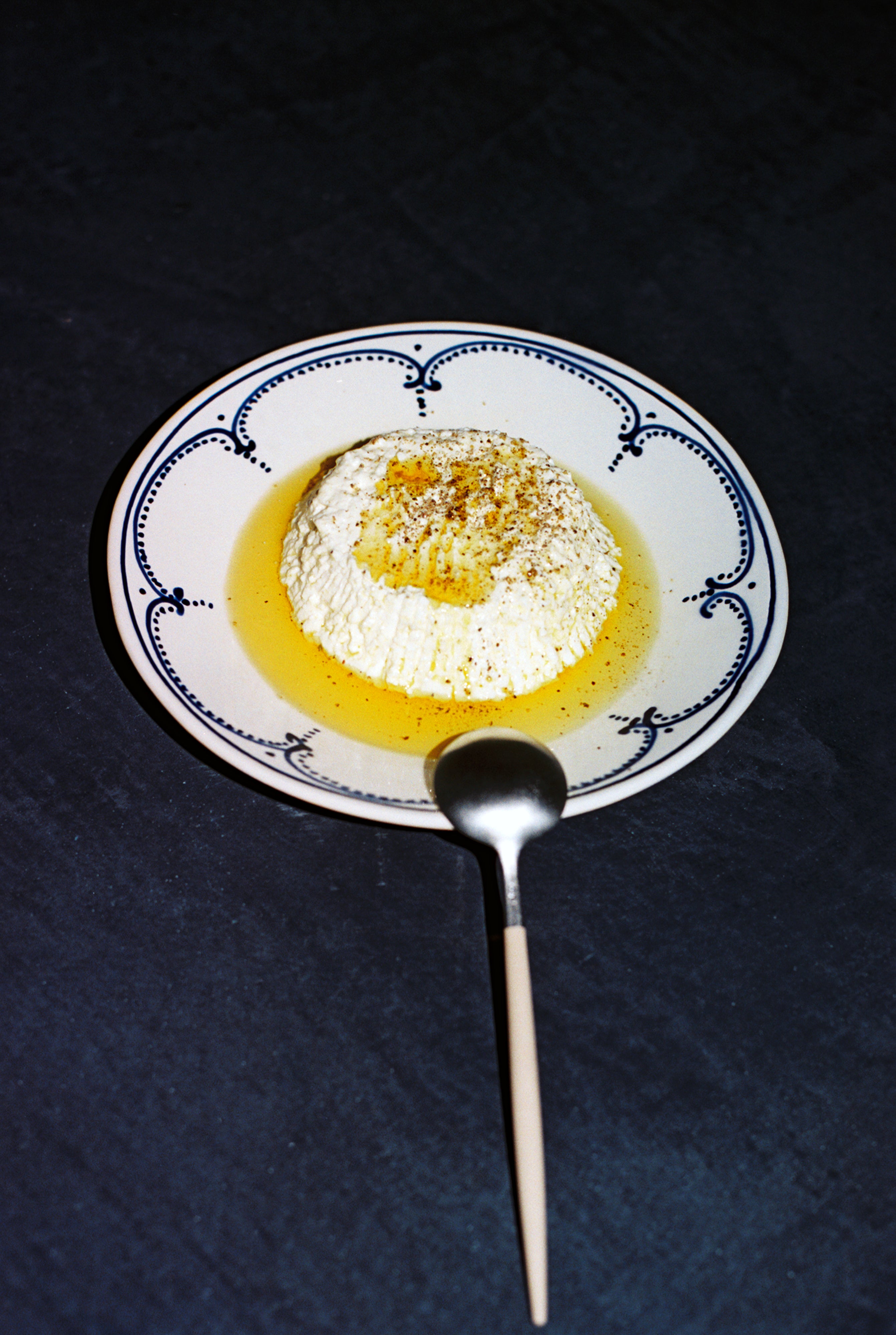 A serving of ricotta cheese with olive oil and seasoning on an Arco Dinner Plate, Set of 4, featuring traditional Portuguese design, with a spoon placed in front.