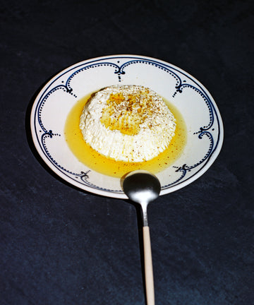 A serving of ricotta cheese with olive oil and seasoning on an Arco Dinner Plate, Set of 4, featuring traditional Portuguese design, with a spoon placed in front.