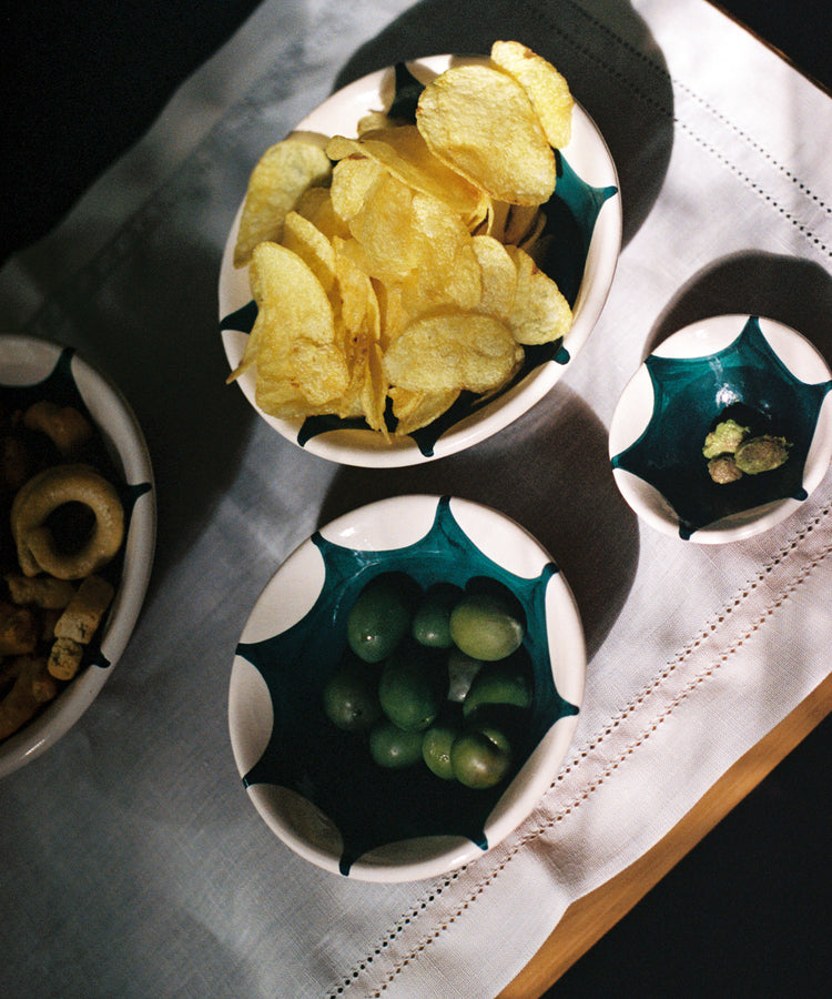 A bowl of potato chips, a bowl of green grapes, a bowl with a few nuts, and a bowl of mixed snacks are artfully arranged on a white cloth, each served in Stella Nesting Bowls that add charm and personality to your table setting.