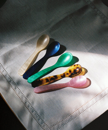 Five Piccolo Spoons—white, blue, green, tortoiseshell, and pink—display design craftsmanship as they lie side by side on a white linen napkin.