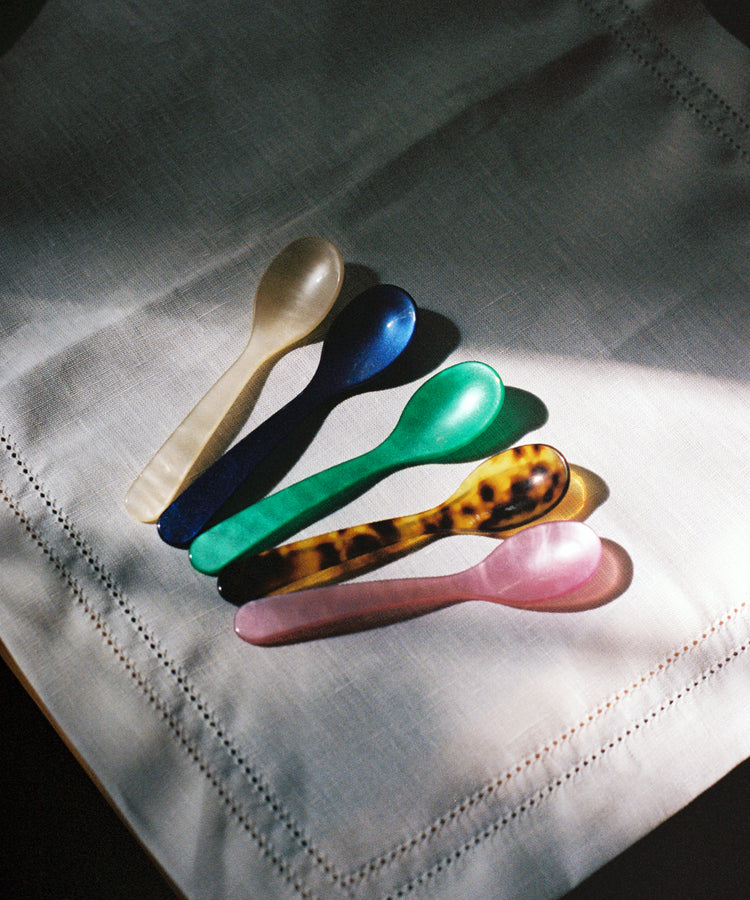 Five Piccolo Spoons—white, blue, green, tortoiseshell, and pink—display design craftsmanship as they lie side by side on a white linen napkin.