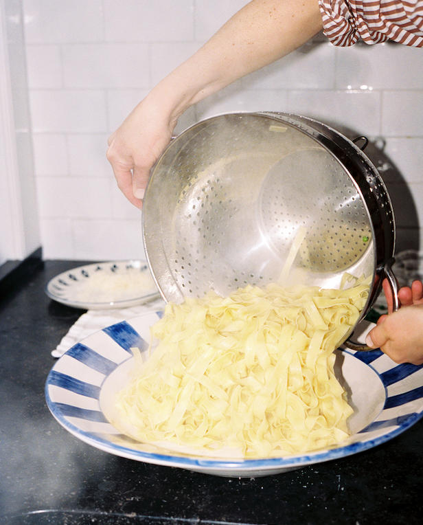 hands pouring pasta from pot onto plate