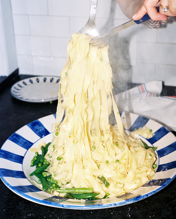 hands tossing pasta in a serving plate