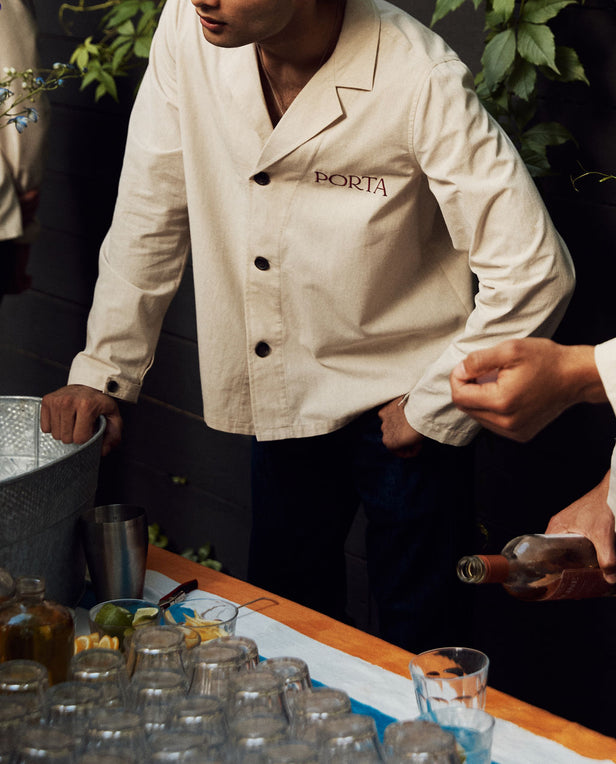Person wearing a 'Porta' jacket at a bar with bottles and glasses.