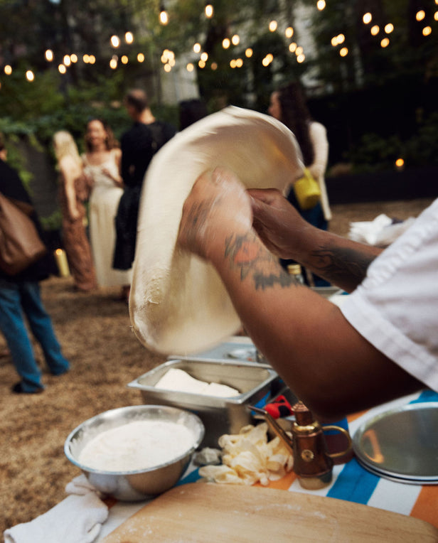 Person making pizza dough at an outdoor event with string lights in the background