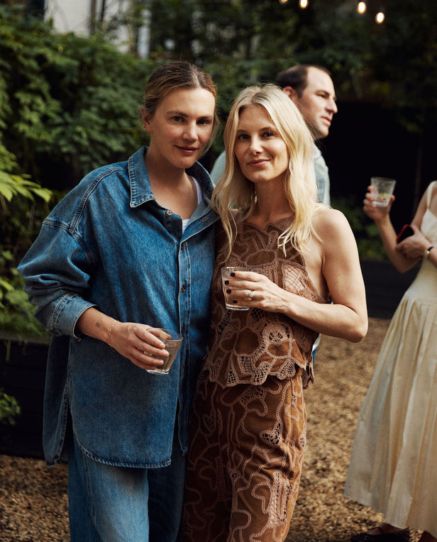 Two women standing outdoors, holding drinks, with a casual setting.