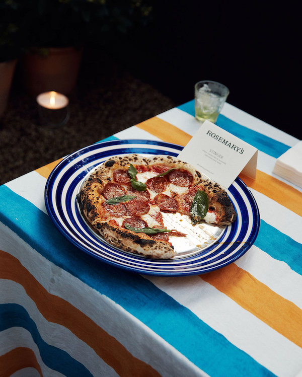 Pizza on a striped tablecloth with a glass of water and a menu in the background