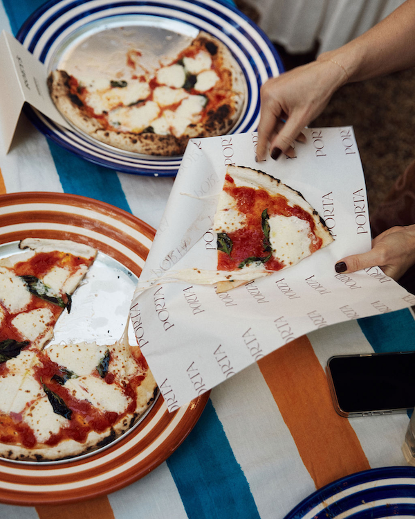 Person holding a pizza box with a small pizza on a striped tablecloth
