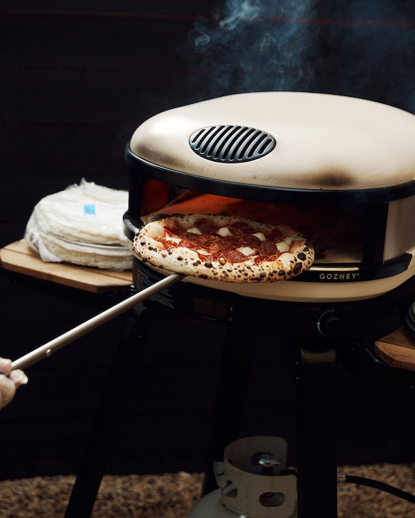 Portable pizza oven with a pizza being cooked inside, on a dark background.