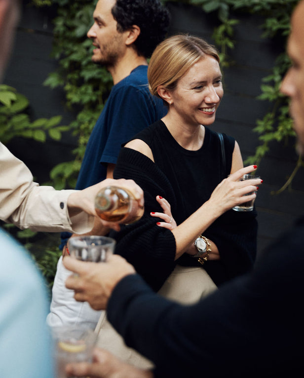 People socializing outdoors with drinks, surrounded by greenery