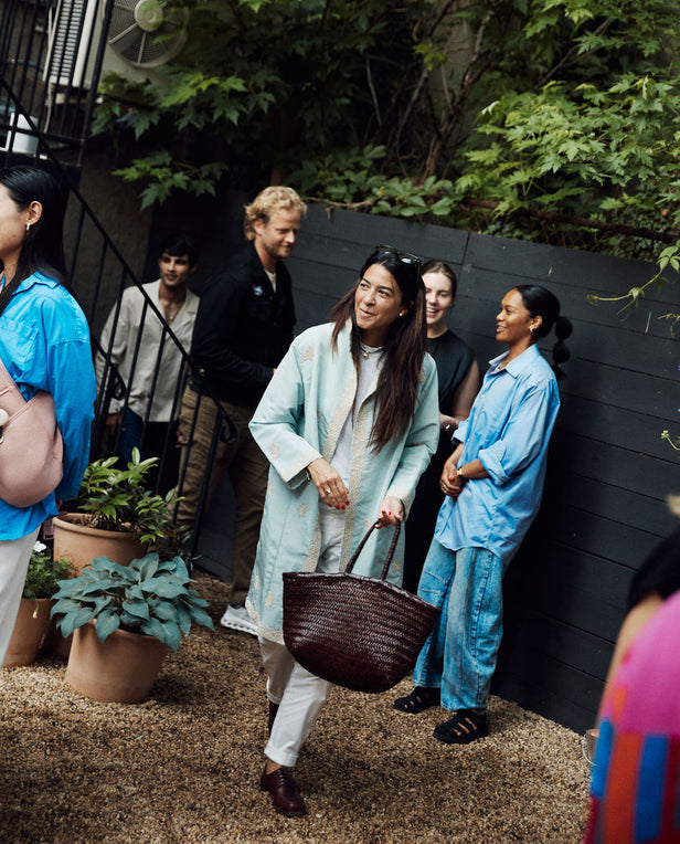 Woman holding a woven basket in an outdoor setting with people and plants around.