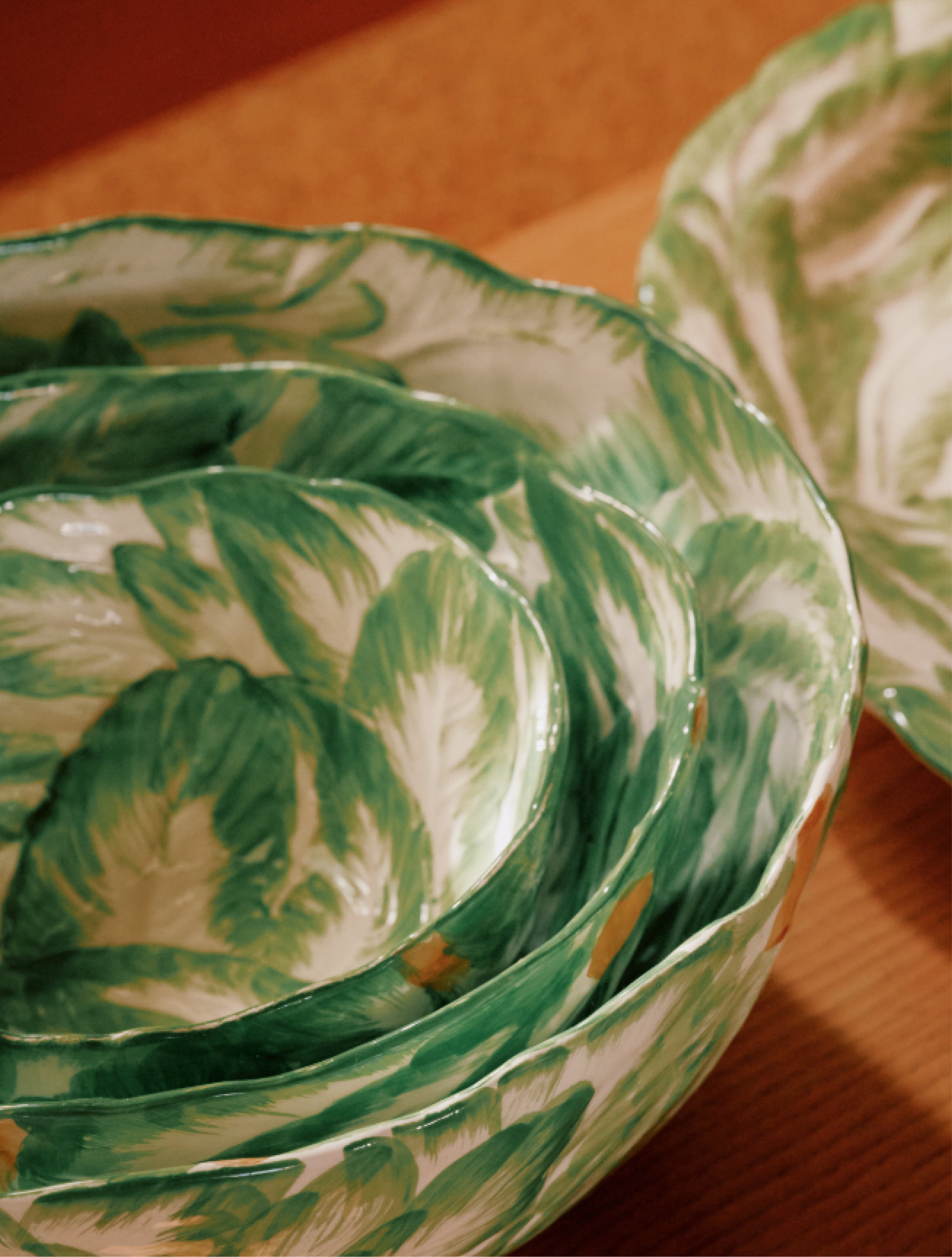 The Nesting Bundle features stacked wood-fired bowls with green and white leaf patterns, resting on a wooden surface next to a matching plate.