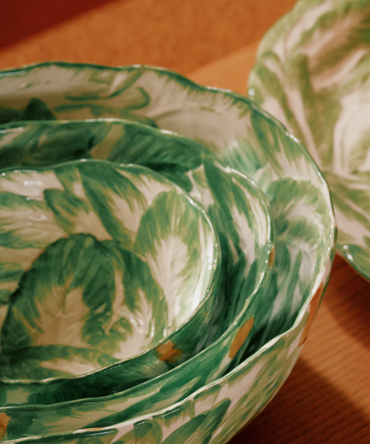 The Nesting Bundle features stacked wood-fired bowls with green and white leaf patterns, resting on a wooden surface next to a matching plate.