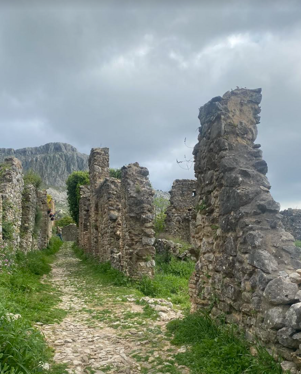 Stone ruins with a rocky path and mountains in the background under cloudy skies.