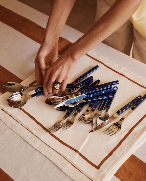 Person arranging blue and silver cutlery on a striped surface