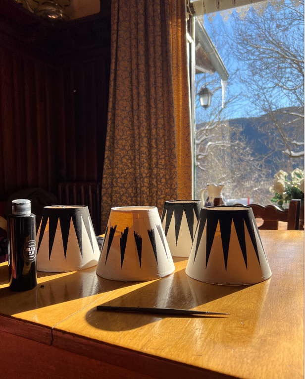 Hand-painted lampshades drying on a wooden table in sunlight