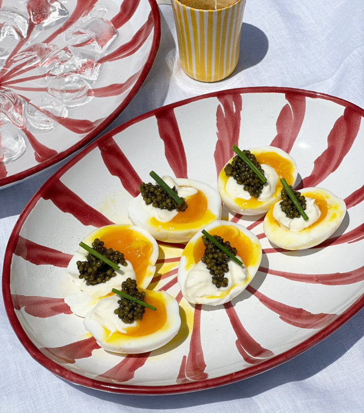 Plate of halved soft-boiled eggs topped with caviar and chives on a red-and-white patterned dish
