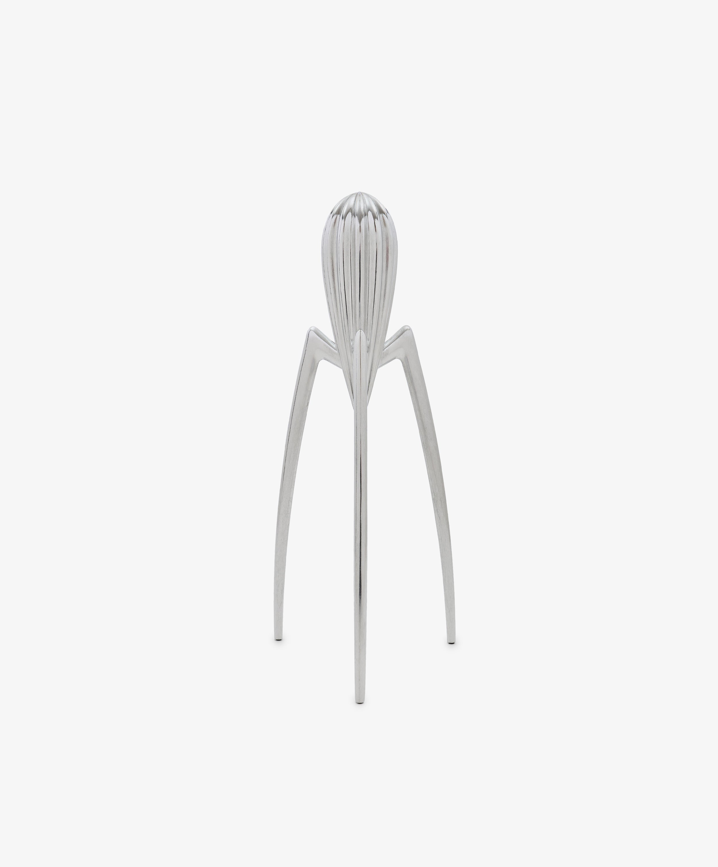 Standing upright on a plain white background, the Juicy Salif Citrus Squeezer by Philippe Starck is an iconic kitchen tool, featuring a silver metal finish with three long legs and a ribbed top designed for juicing citrus fruits.