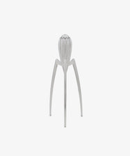 Standing upright on a plain white background, the Juicy Salif Citrus Squeezer by Philippe Starck is an iconic kitchen tool, featuring a silver metal finish with three long legs and a ribbed top designed for juicing citrus fruits.
