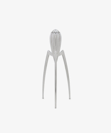 Standing upright on a plain white background, the Juicy Salif Citrus Squeezer by Philippe Starck is an iconic kitchen tool, featuring a silver metal finish with three long legs and a ribbed top designed for juicing citrus fruits.