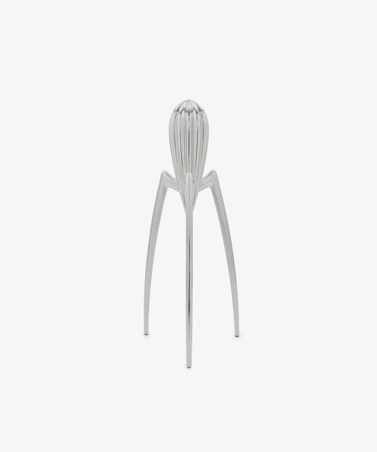 Standing upright on a plain white background, the Juicy Salif Citrus Squeezer by Philippe Starck is an iconic kitchen tool, featuring a silver metal finish with three long legs and a ribbed top designed for juicing citrus fruits.