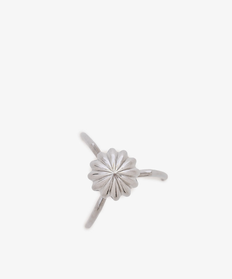 A silver ring inspired by the sculptural lines of the Juicy Salif Citrus Squeezer, featuring a central flower-shaped design with a ridged texture, set on a thin band against a white background.