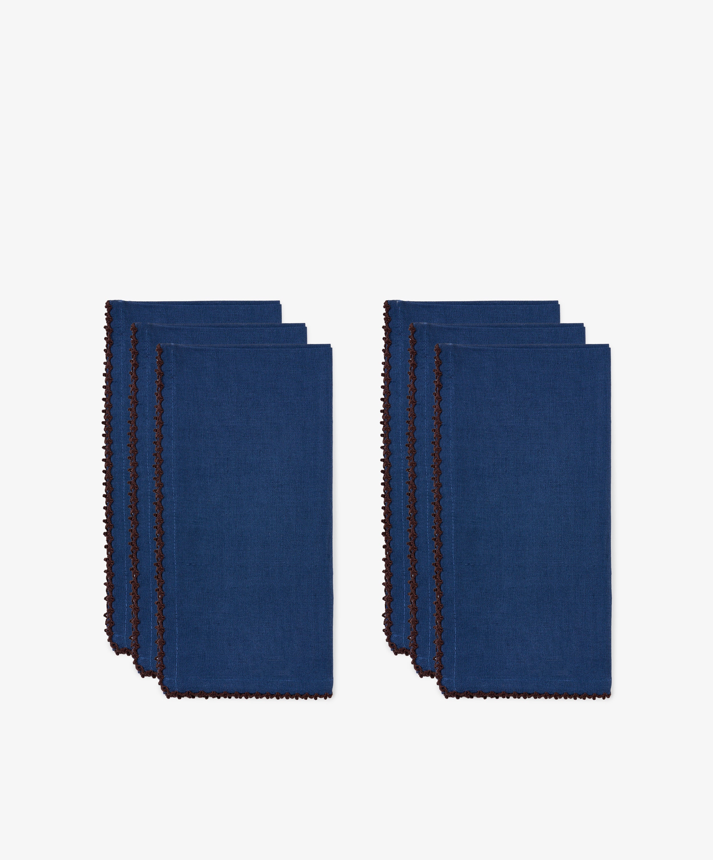 Two sets of six neatly folded indigo blue Nico Napkins with brown edges, arranged side by side on a white background, each classic linen napkin is designed to add timeless elegance to your dining experience.