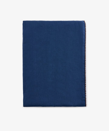 A neatly folded, rectangular Nico Tablecloth in indigo blue linen with a clean, simple appearance and hand-finished edges, displayed against a plain white background.