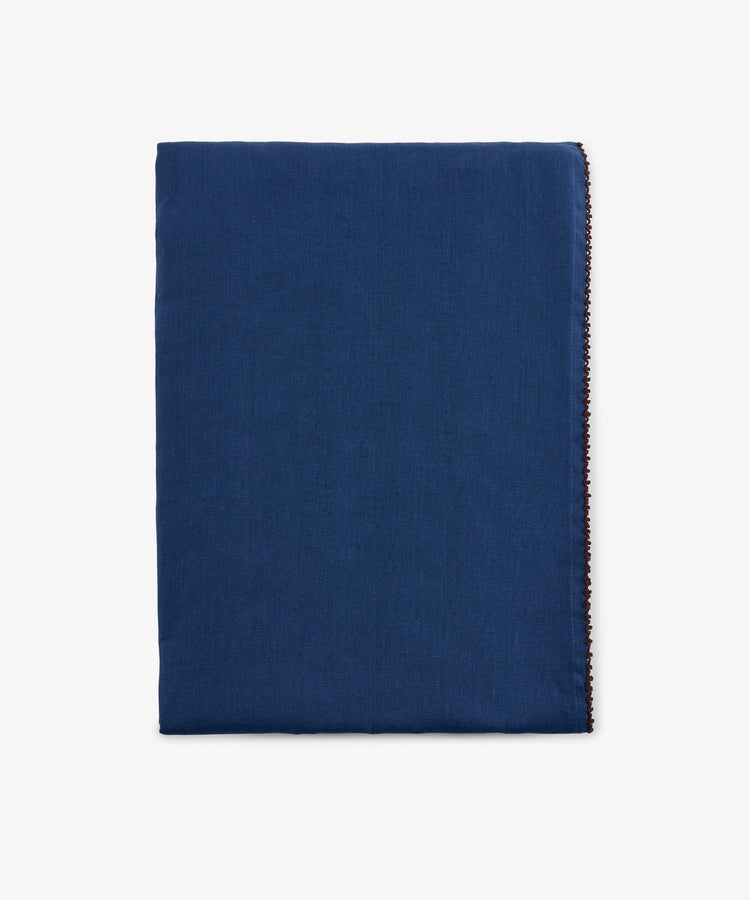 A neatly folded, rectangular Nico Tablecloth in indigo blue linen with a clean, simple appearance and hand-finished edges, displayed against a plain white background.