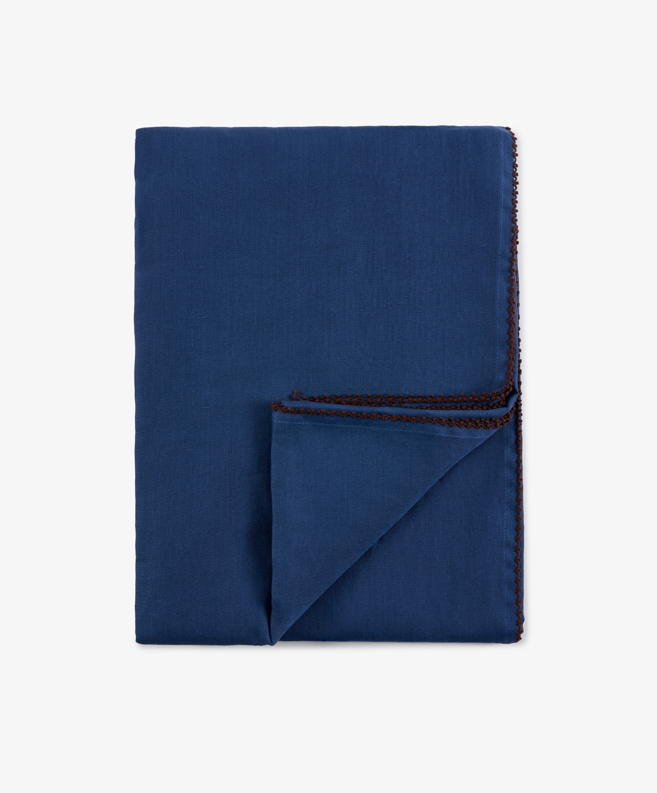 A neatly folded Nico Tablecloth in indigo blue with hand-finished brown stitching along the edges, displayed on a plain white background.