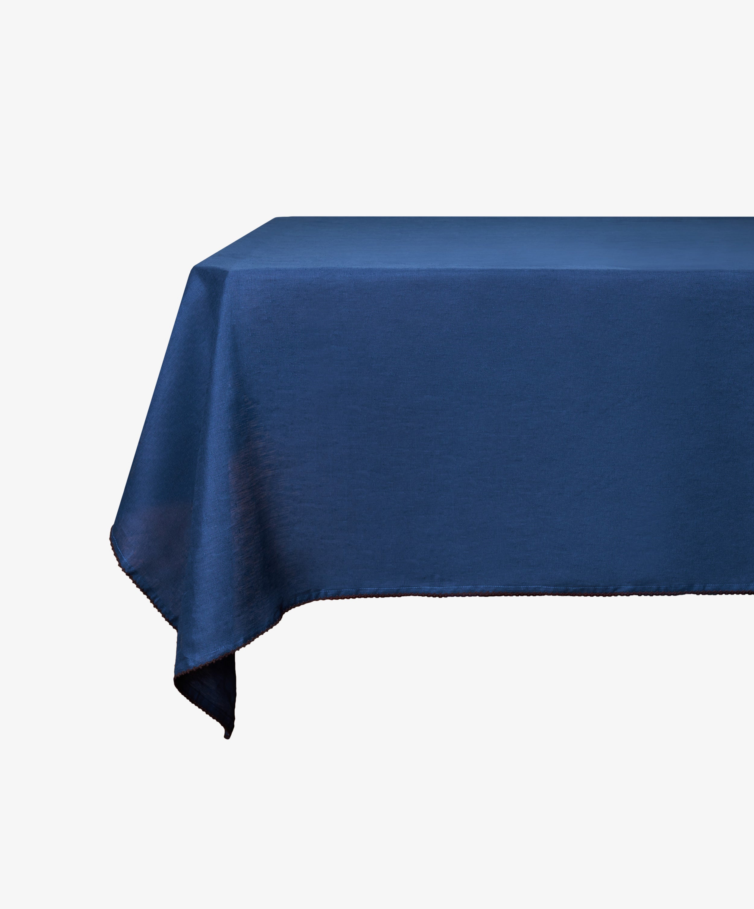 A rectangular table covered with the Nico Tablecloth, a hand-finished linen piece in indigo blue, set against a white background.