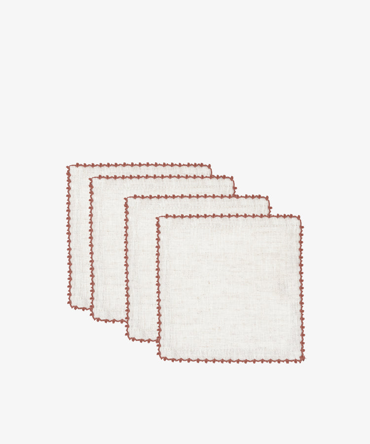 The Nico Cocktail Napkin, Set of 4 features white linen napkins with red stitched borders, hand-finished in Portugal, neatly stacked against a plain white background.