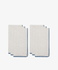 Six folded Nico Napkins in beige linen with blue stitched edges are stacked against a white background, perfect for elegant dining or as stylish modern table linens.