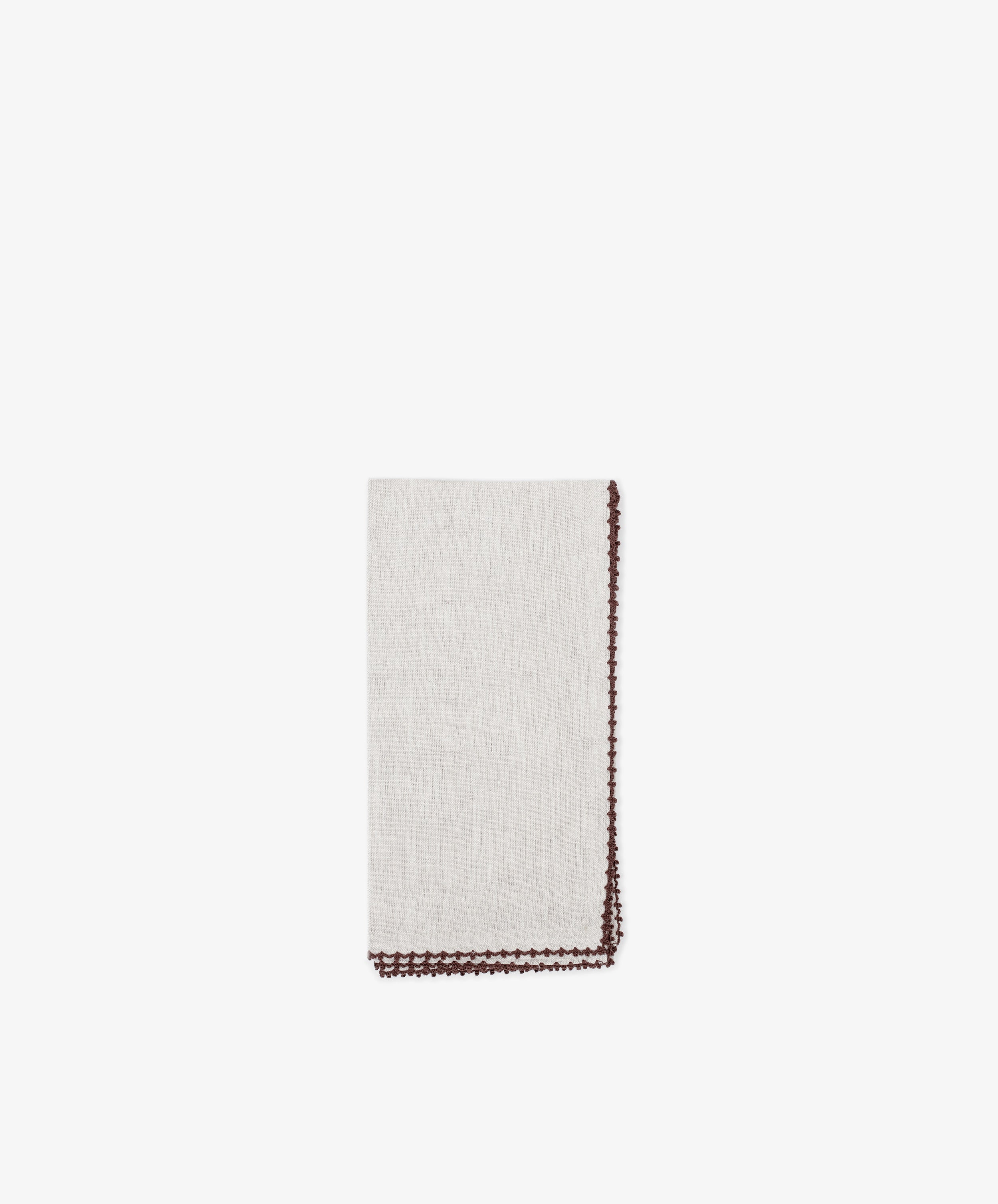 The Nico Napkin, Set of 6, features light beige linen with a decorative brown border and subtle contrast stitching, shown neatly folded on a plain white background.