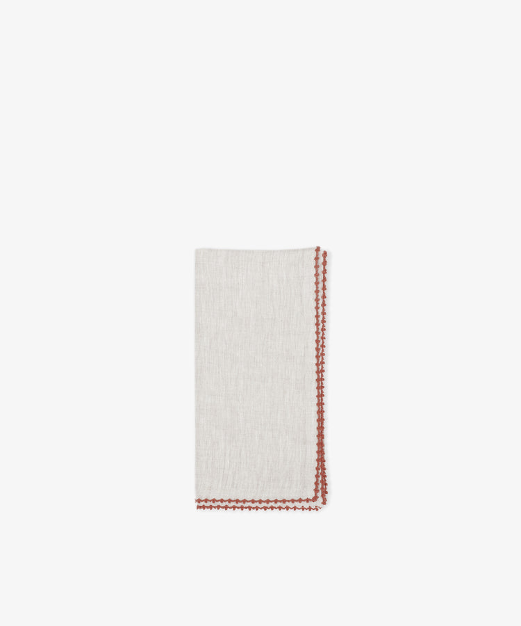 The Nico Napkin, Set of 6, features folded light beige linen napkins with bold red contrast stitching along the edges, displayed on a plain white background.