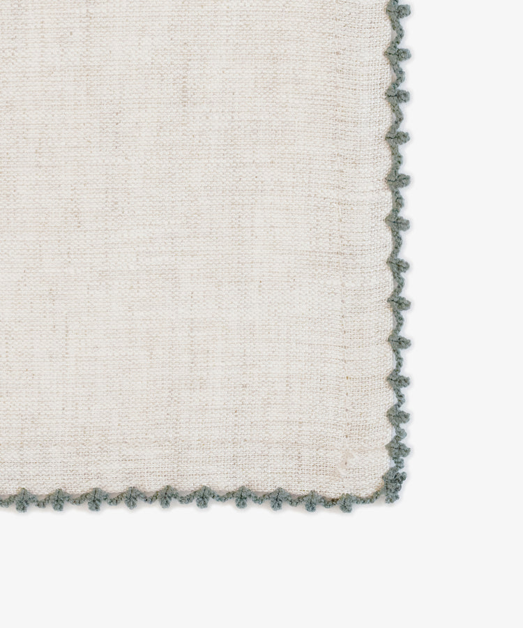 A close-up of the Nico Napkin, Set of 6, in beige linen with scalloped green lace trim—ideal for modern table settings—displayed against a white background.